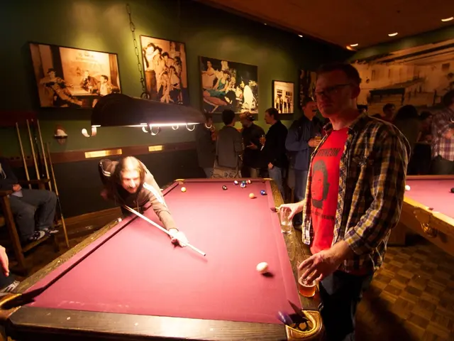 The picture is inside a club, there are two snooker tables, on the first table two people are...